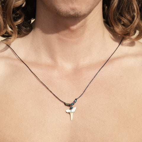 Surfer with a real shark tooth necklace  on, featuring a fossil shark tooth as the central pendant, surrounded by glass seed beads on a black cord